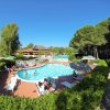 Piscina all'aperto con persone su sdraio, alberi circostanti.