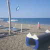 Una spiaggia con ombrelloni, lettini, una bandiera blu alzata e un tunnel-gioco nero sulla sabbia.