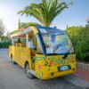 Un veicolo giallo decorato con disegni colorati, parcheggiato vicino a palme lungo una strada.