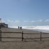 Spiaggia sabbiosa con persone che camminano, cielo limpido e onde in lontananza.