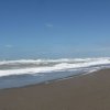 Spiaggia deserta con onde e cielo azzurro con poche nuvole.