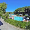 Una grande piscina circondata da alberi e persone che si rilassano, con un cielo blu limpido.