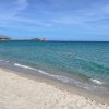 Spiaggia sabbiosa con mare calmo e acqua turchese sotto un cielo azzurro.