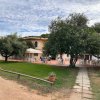 Edificio bianco con veranda, sedie e tavoli all'aperto, circondato da alberi.