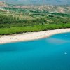 Spiaggia con sabbia chiara, mare azzurro e vegetazione verde.