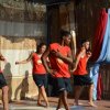 Gruppo di giovani danza su un palco. Indossano canotte rosse e pantaloncini neri.