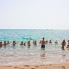 Persone nuotano nel mare vicino alla riva, illuminate dal sole.