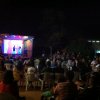 Spettatori seduti guardano uno spettacolo su un palco illuminato di notte.