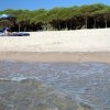 Spiaggia con ombrelloni blu, persona su lettino e mare calmo in primo piano.
