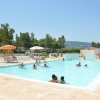 Una piscina all'aperto con persone che nuotano. Sullo sfondo, alberi e ombrelloni.