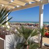 Veduta di una spiaggia affollata con palme e tavoli all'ombra.