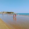 Persone camminano sulla battigia di una spiaggia sabbiosa.