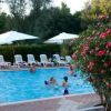 Piscina con giocatori, sedie a sdraio e ombrelloni bianchi. Fiori rossi in primo piano.