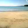 Una spiaggia sabbiosa con mare calmo e scogli in lontananza.