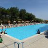 Una grande piscina con lettini, ombrelloni arancioni e alberi sullo sfondo.