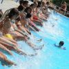 Persone sedute sul bordo di una piscina, schizzando acqua con i piedi.