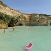 Persone nuotano in un mare turchese vicino a scogliere rocciose.
