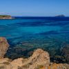 Scogliera rocciosa e mare turchese sotto un cielo blu limpido.