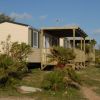 Casa mobile con veranda in legno, circondata da piccoli cespugli e palme.