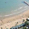 Spiaggia sabbiosa con ombrelloni, bagnanti e un molo di pietre.