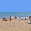 Spiaggia sabbiosa con persone che si rilassano e nuotano.