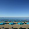 Spiaggia sabbiosa con ombrelloni blu e mare calmo.