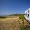 Un camper parcheggiato su un prato con vista su una recinzione e colline in lontananza.