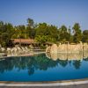Piscina all'aperto con rocce decorative, circondata da lettini e alberi.
