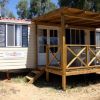 Roulotte beige con veranda in legno e finestre con persiane blu, immersa tra alberi.