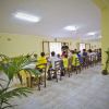 Una sala con bambini seduti a tavola. Pareti gialle e pavimento piastrellato.
