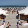 Spiaggia con file di ombrelloni e sdraio, tra due tendoni bianchi con tavoli.
