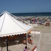 Una spiaggia affollata con lettini e un grande gazebo bianco vicino al mare.