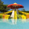 Scivoli gialli sotto un fungo spruzzante in una piscina per bambini.