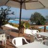 Tavoli e sedie bianche sotto ombrelloni, vista piscina e mare.