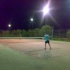 Campo da tennis illuminato di notte con tre persone che giocano.