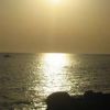 Sole al tramonto che riflette sull'acqua del mare, con silhouette di scogli.