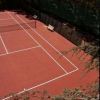 Campo da tennis in terra rossa con panchina e rete.