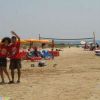 Due persone sorridenti su una spiaggia sabbiosa, ombrelloni arancioni e mare sullo sfondo.