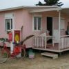 Casetta rosa con veranda bianca e bicicletta rossa parcheggiata davanti.