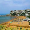 Spiaggia con ombrelloni colorati e case bianche su una collina.
