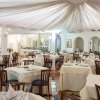 Sala con tavoli quadrati apparecchiati e soffitto drappeggiato.