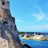 Torre di pietra su scogliera con vista sul mare blu.