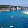 Mare azzurro con barche vicino a scogliere.