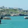 Scogliera verde e mare blu con città sullo sfondo.