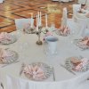 Tavolo rotondo apparecchiato con tovaglia bianca e tovaglioli rosa.