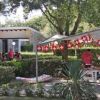 Alcune persone sono sedute sotto un gazebo decorato con bandierine, circondato da alberi e cespugli.