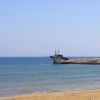 Spiaggia sabbiosa con mare calmo e struttura di legno sul promontorio.