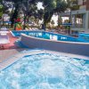 Area esterna con piscina e vasca idromassaggio circondate da lettini e alberi.