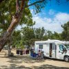 Camper parcheggiato tra alberi e persone sedute all'esterno.