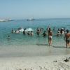 Spiaggia con persone che giocano in acqua, barca a vela in lontananza.